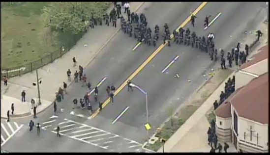 A line of police advances on a cluster of youth.
